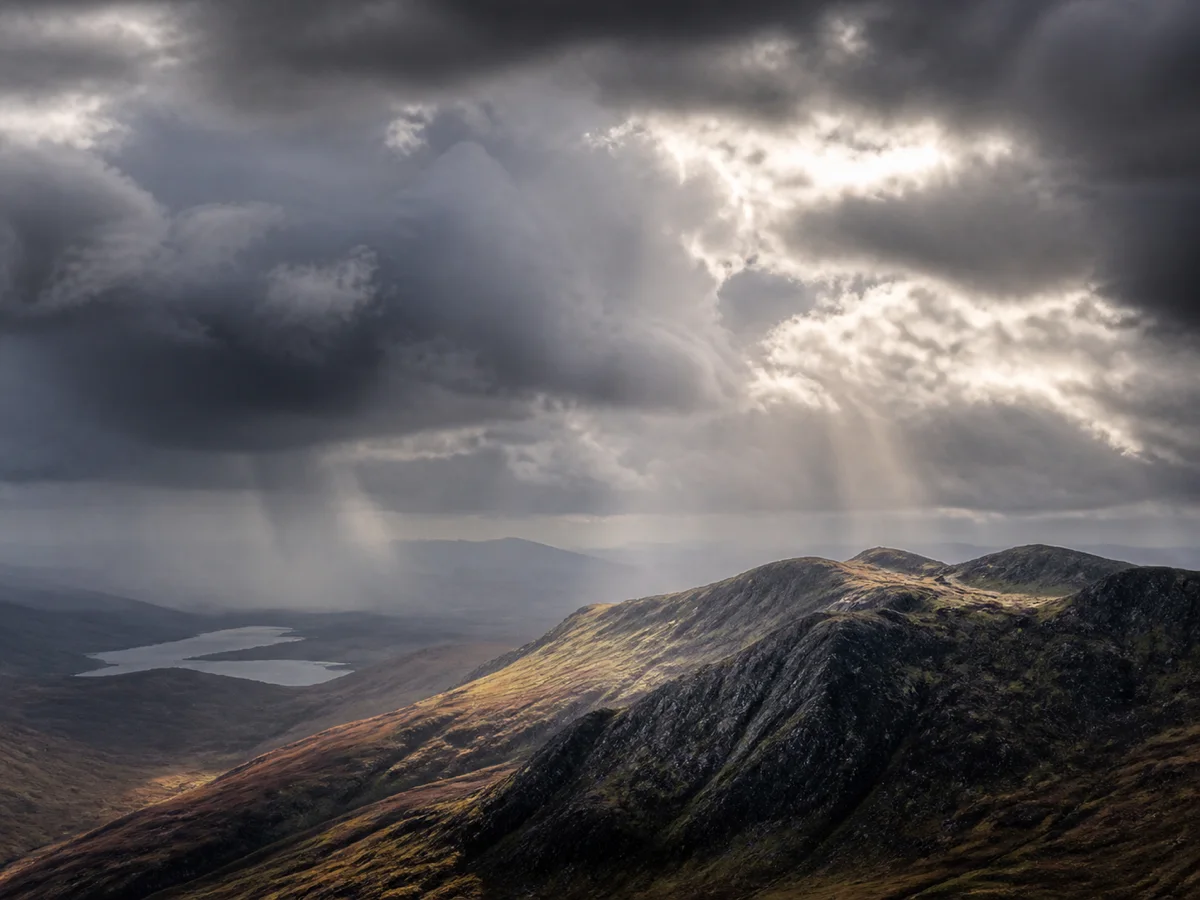 Sunlight breaking through storm clouds onto a mountain ridge